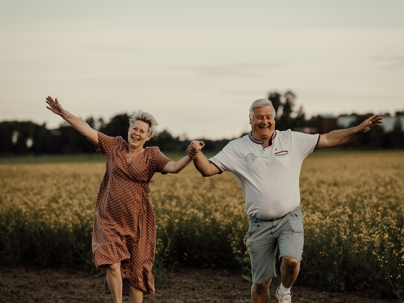 An older couple running joyfully through a sunlit field