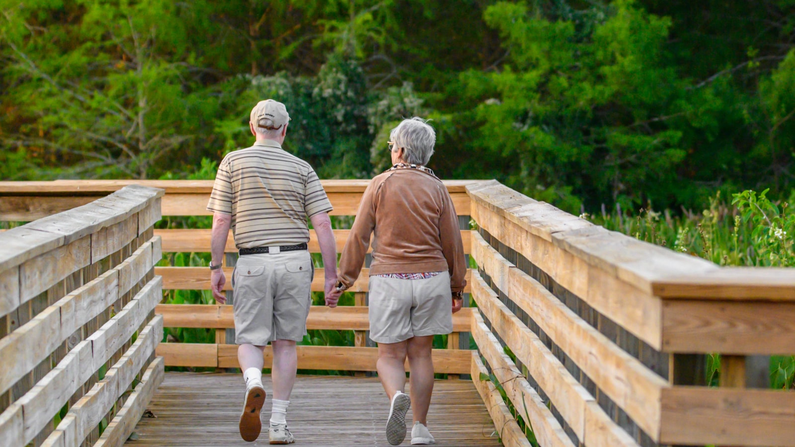 An older couple walks hand-in-hand across a wooden bridge